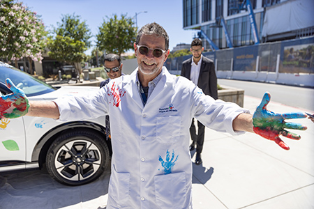A person in a white coat holds out his painted hands.